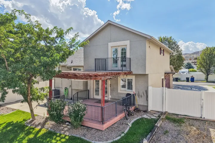 Rear exterior featuring a ground-level deck with a pergola, a second-story balcony with French doors, and a private fenced yard