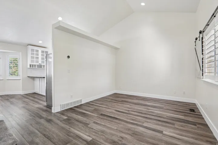 Vaulted ceiling with recessed lighting, wood-finish flooring, white plantation shutters, and stainless steel refrigerator