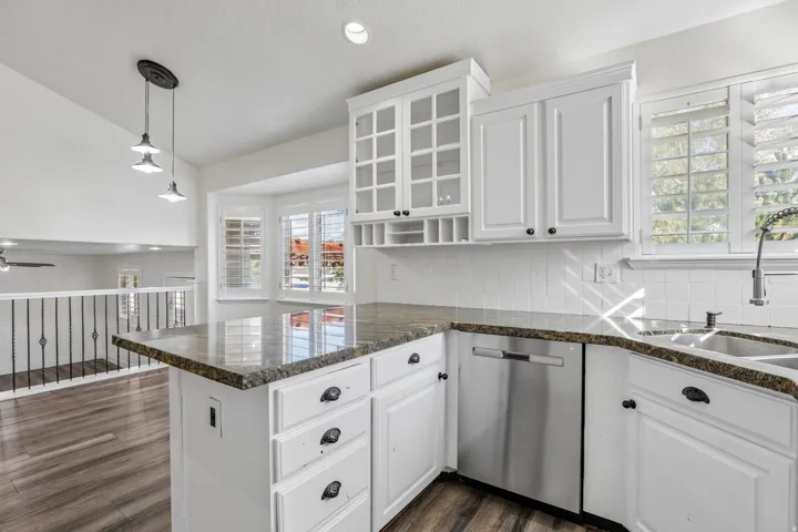 White cabinetry with black hardware, stone countertops, stainless steel dishwasher, and a white subway tile backsplash