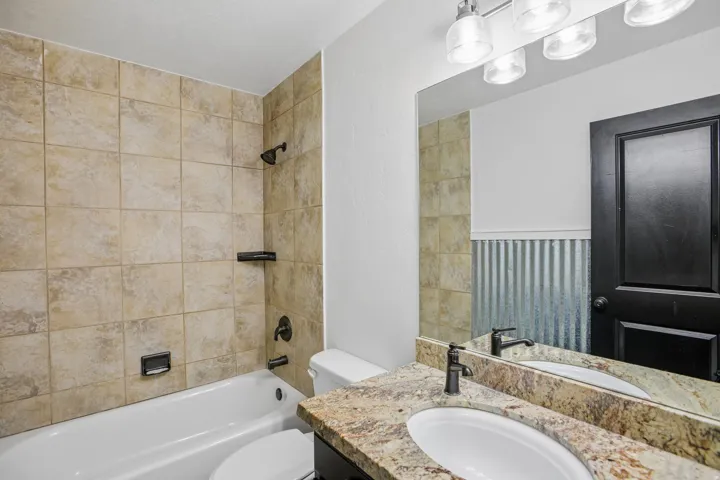 Bathtub with tile surround, vanity with stone countertop, drop-in sink, and wall-mounted mirror