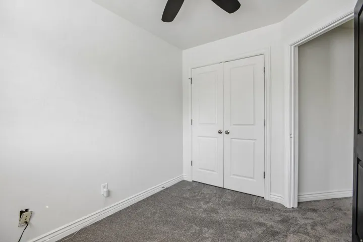 Textured carpeting, white walls, double bi-fold closet doors, and ceiling fan