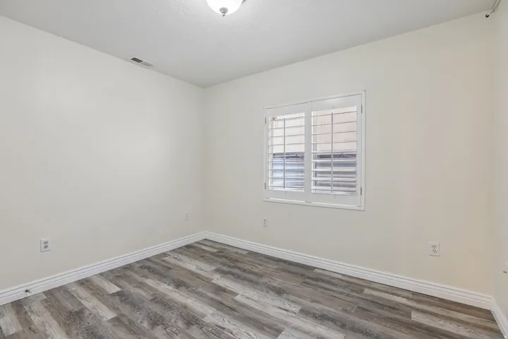 Wood-finish flooring, white walls, white trim, window with white plantation shutters, and a ceiling-mounted light fixture