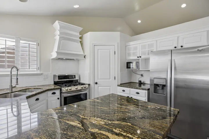 Kitchen featuring white cabinetry, dark stone countertops, stainless steel appliances, and a double basin sink