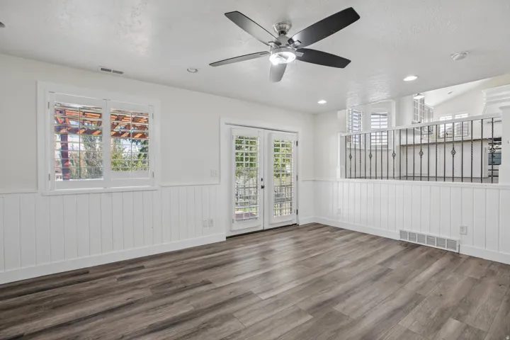 Wood-finish flooring, white wainscoting, and a ceiling fan with integrated lighting