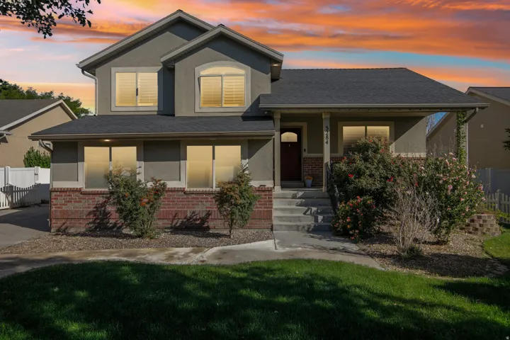 Stucco and brick facade with a dark shingle roof, concrete porch, and mature landscaping