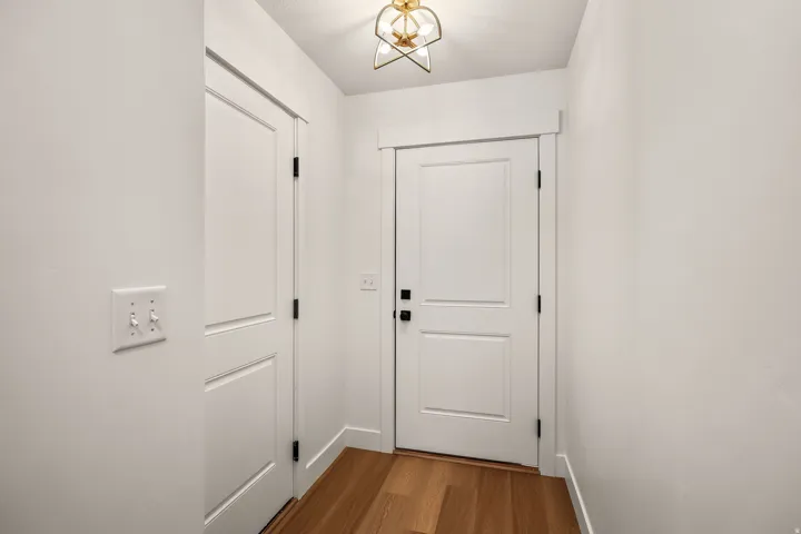 Wood-finish flooring with white baseboards, white paneled doors, and a decorative ceiling light fixture
