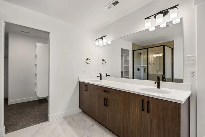 Dual vanity with wood-finish cabinetry, white countertops, and matte black fixtures