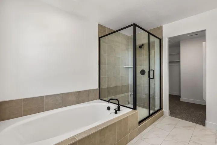 Soaking tub with matte black fixtures, tile surround, and a glass-enclosed shower with matte black frame