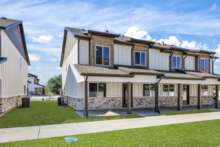 Modern townhome exterior featuring a stone and board-and-batten facade, covered front porch, dark-framed windows, and a dark shingle roof