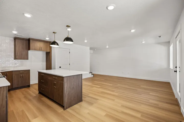 Kitchen island with a white countertop, recessed lighting, wood-finish flooring, dark wood cabinetry, and pendant light fixtures