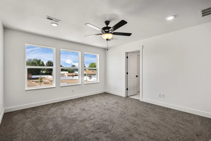 Three large windows, a ceiling fan with integrated lighting, recessed lighting, and grey carpeting