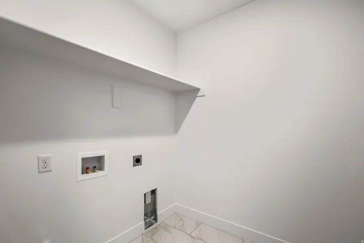 Wall-mounted shelving, electrical outlets, washer hookups, dryer vent, and patterned floor tiling