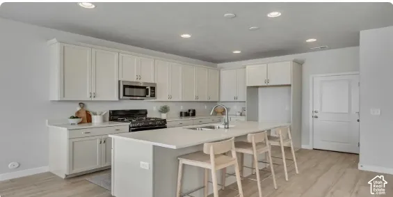 Modern kitchen featuring white cabinetry, stainless steel microwave, gas range, and a central island with an undermount sink. This home is to be built. Pictures are of a similar home.