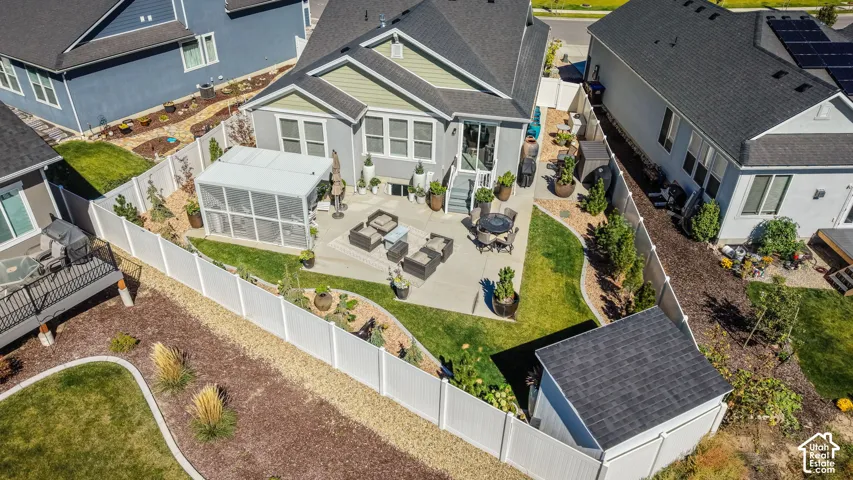 Expansive concrete patio with a detached sunroom, surrounded by a manicured lawn and mature landscaping, and an additional shed structure
