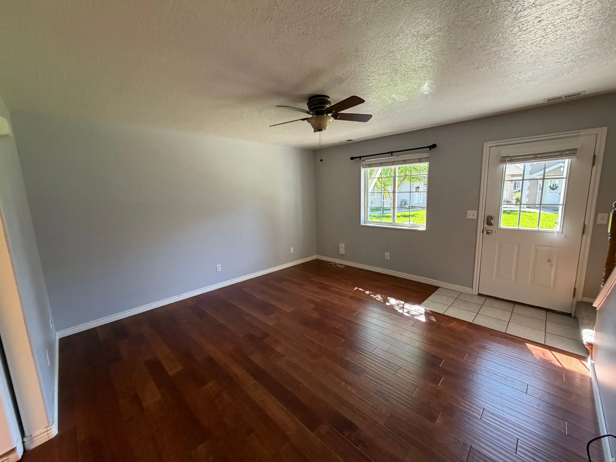 Wood-finish flooring, ceiling fan, white paneled door with window, and a window with blinds