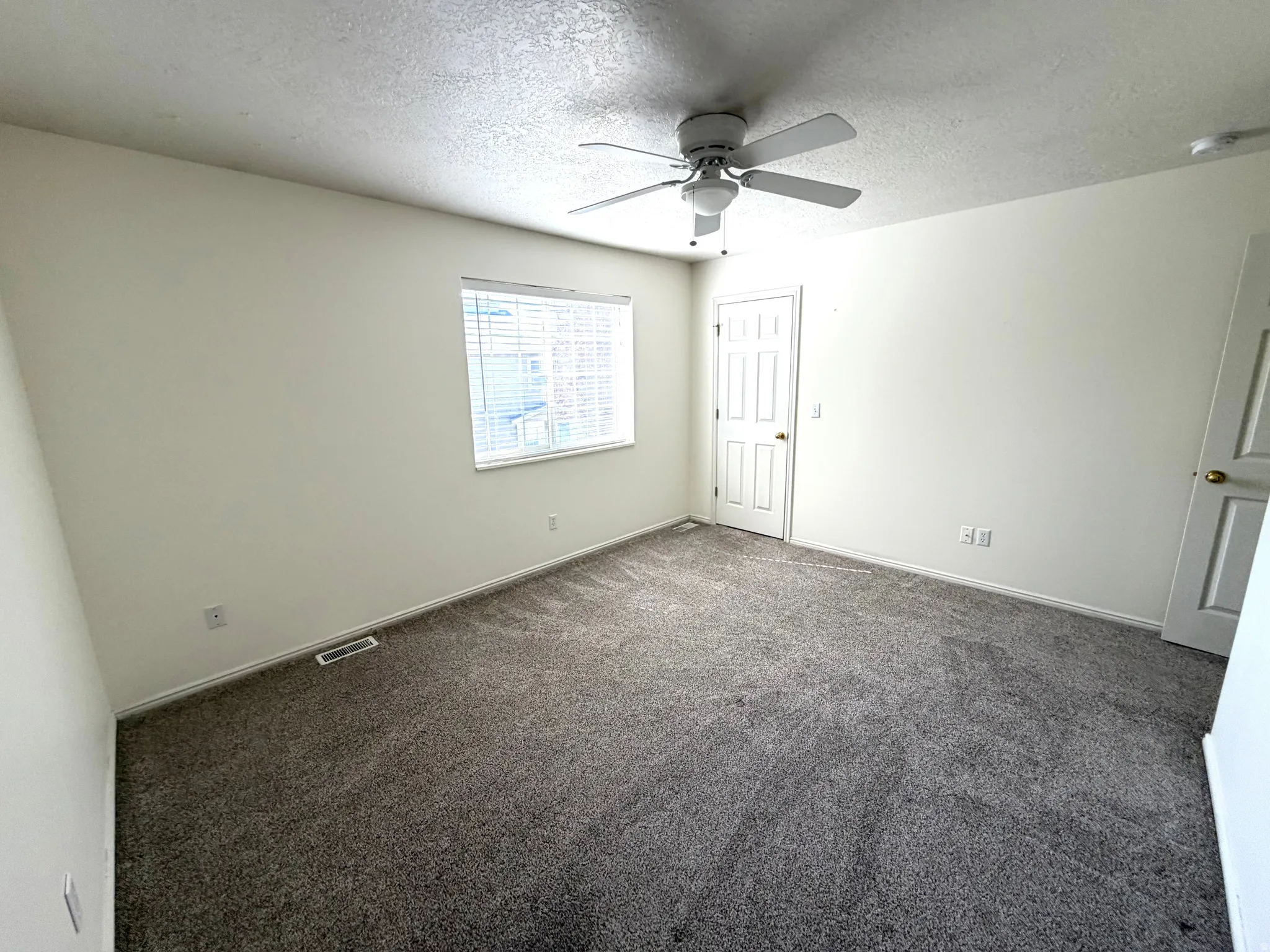 Neutral-toned carpeting, white interior walls, and a ceiling fan with light fixture