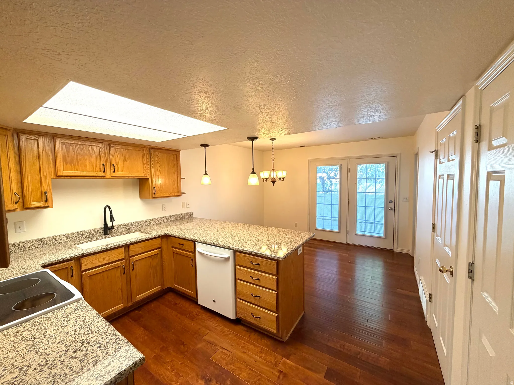Kitchen featuring wood cabinetry, granite-style countertops, wood-finish flooring, and a skylight