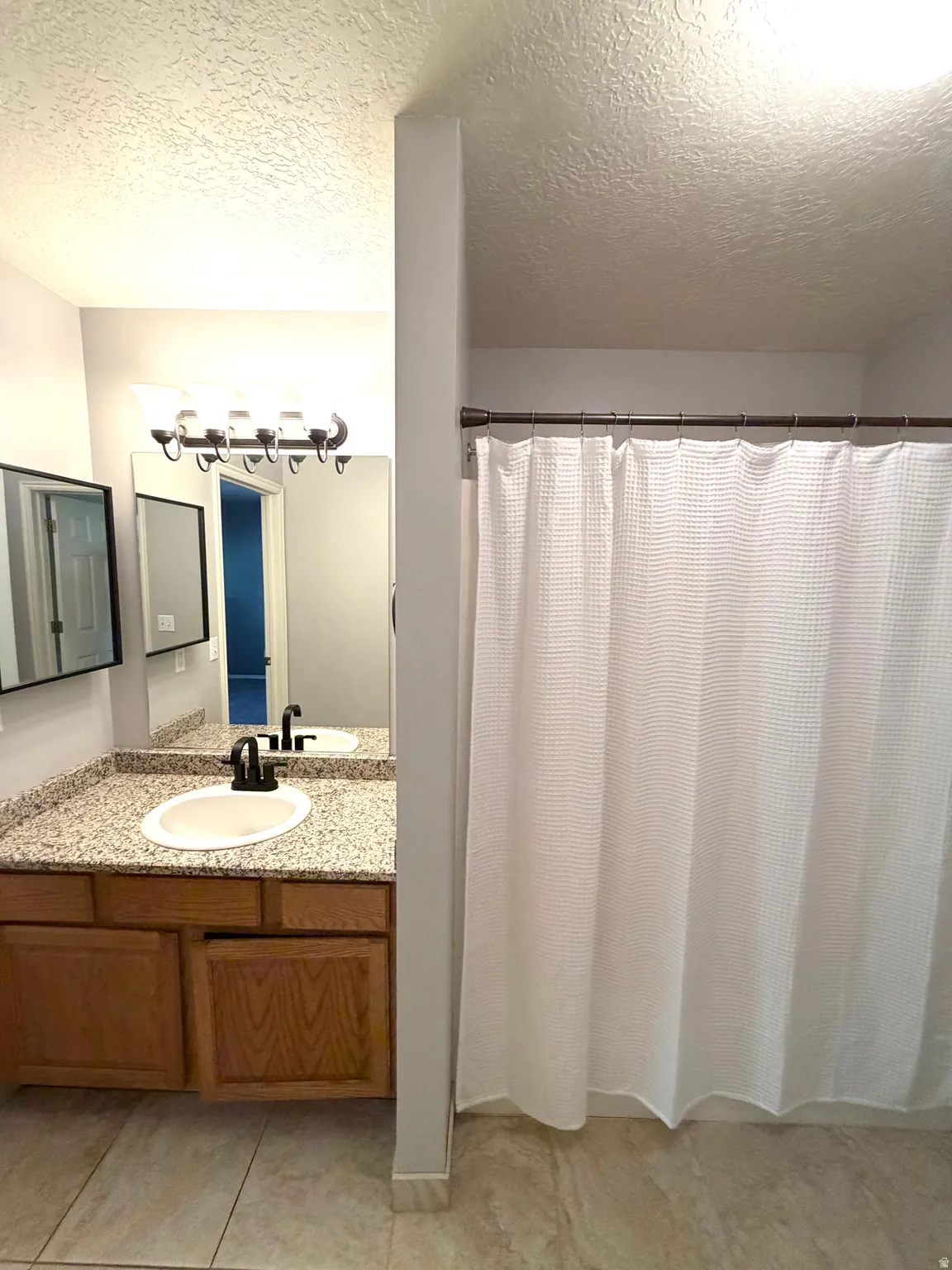 Wood-finish vanity with an undermount sink and speckled countertop, black-finish faucet, and a wall-mounted mirror