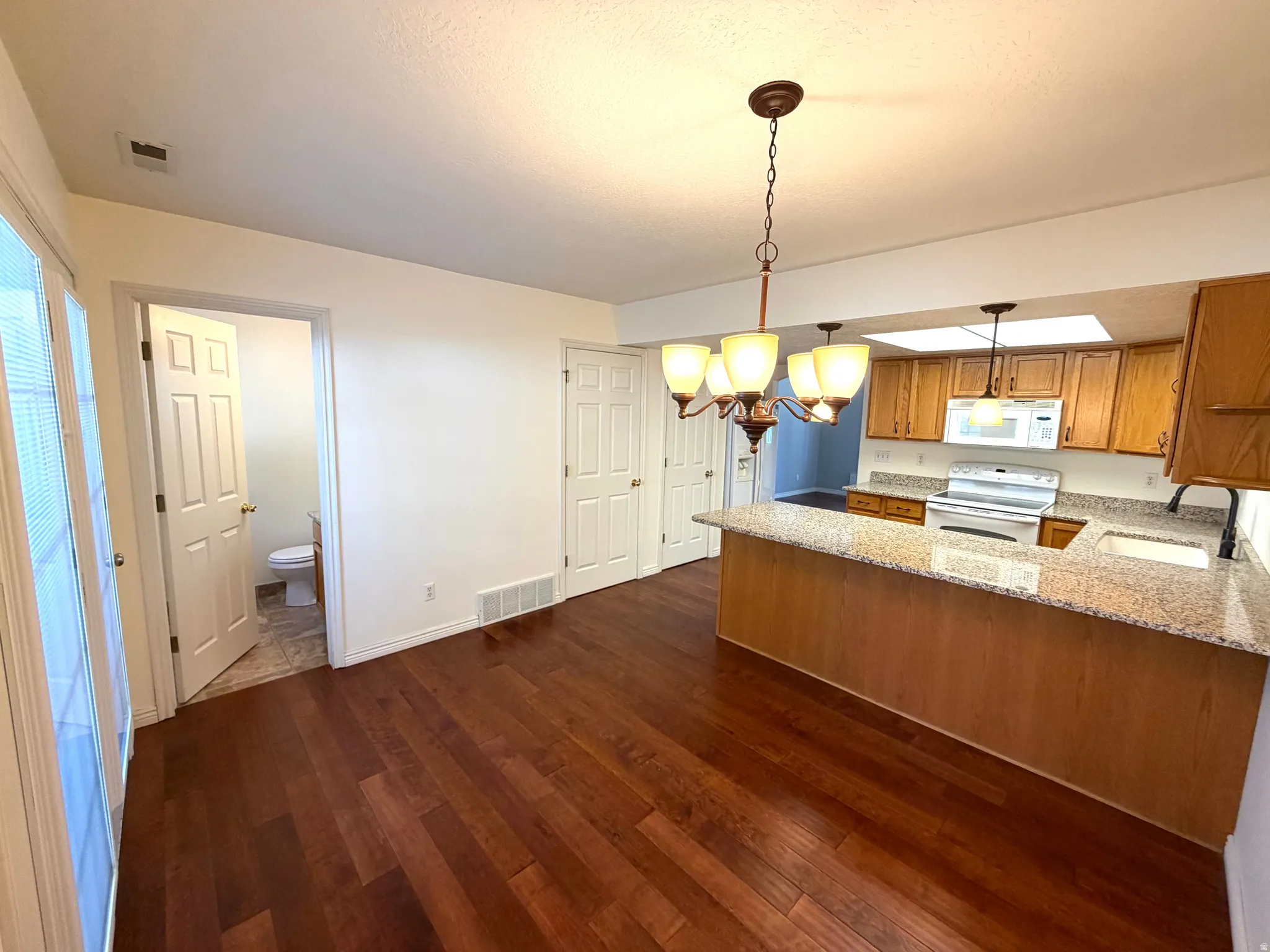 Wood-finish flooring throughout, kitchen with light wood cabinetry, white appliances, and granite-style countertops