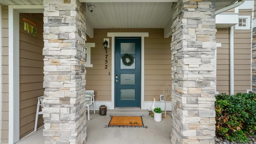 Inviting front entrance featuring stacked stone pillars, a teal entry door with frosted glass panels, and tan siding