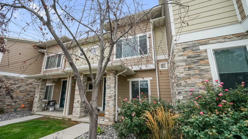 Multi-level townhome featuring stone and horizontal siding exterior, prominent front entry with covered porch, and layered landscaping with mature shrubbery