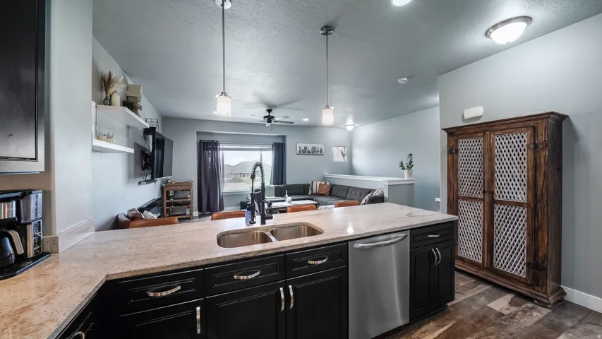 Island kitchen featuring a double basin sink, granite countertop, dark wood-finish cabinetry, and stainless steel dishwasher