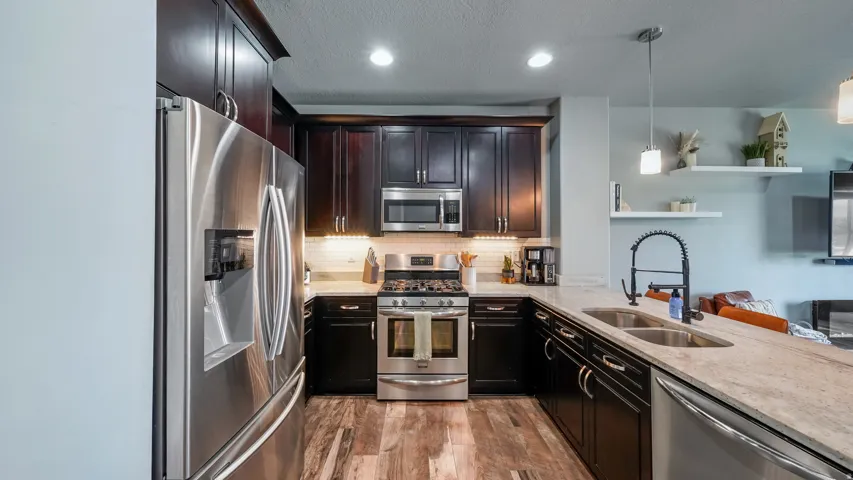 Stainless steel appliances, rich wood-finish cabinetry, light-toned countertops, wood-finish flooring, and a double basin sink with a black faucet