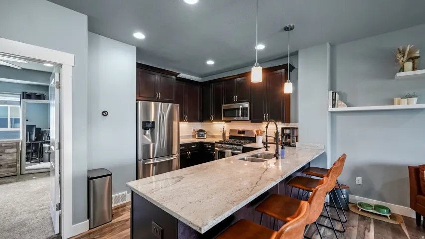 Kitchen with dark wood cabinetry, stainless steel appliances, a stone countertop island, and wood-finish flooring