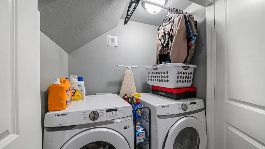 Built-in overhead clothes hanging rod, built-in overhead light fixture, white front-loading washing machine, white front-loading dryer, white paneled door