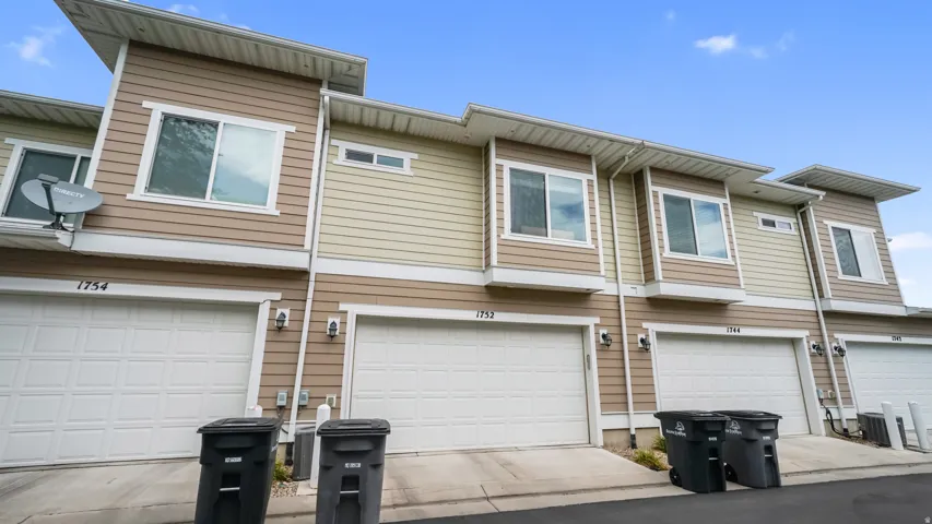 Multi-unit exterior featuring tan siding, white garage doors, and white-framed windows