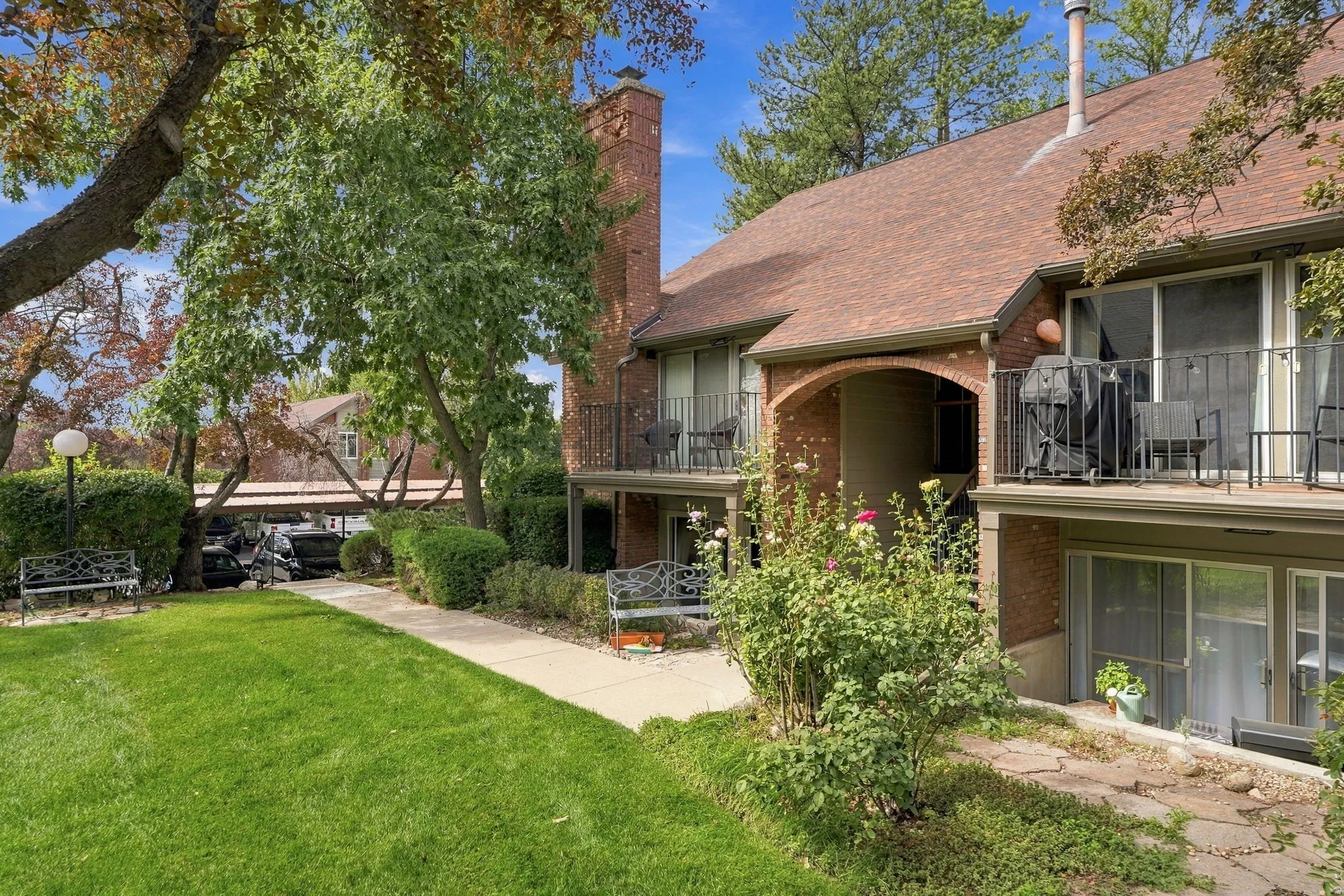 Brick exterior with multiple balconies, mature landscaping, and a covered parking structure