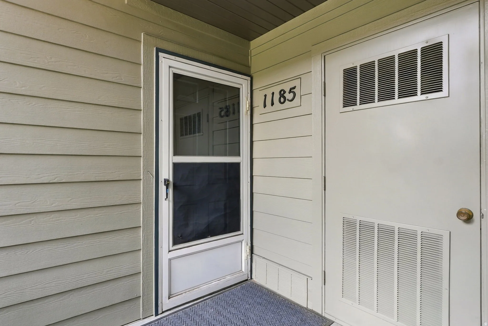 Panel siding exterior with a screen door and an entry door featuring upper and lower louvered panels