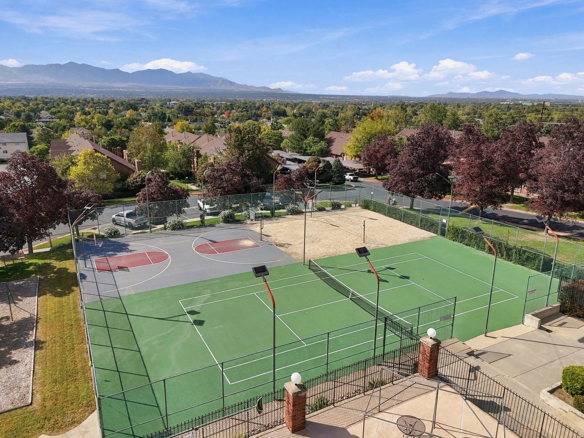 Outdoor basketball court, two tennis courts, sand volleyball court, mountain backdrop, and surrounding green spaces