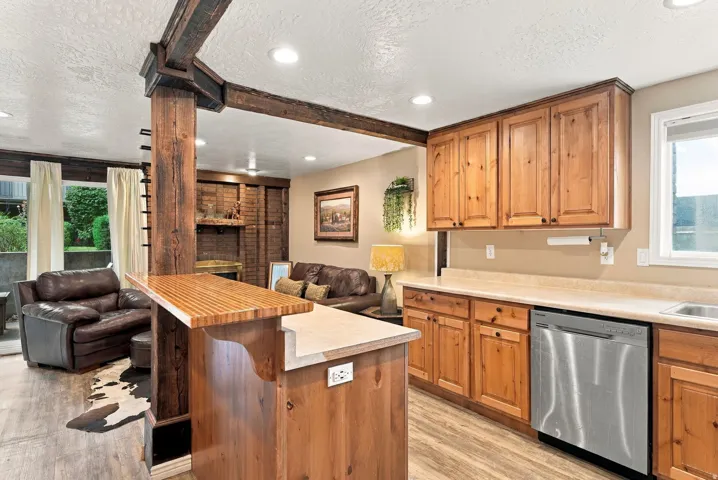 Wood-finish flooring, exposed wood beams, wood cabinetry, stainless steel dishwasher, and a built-in counter bar