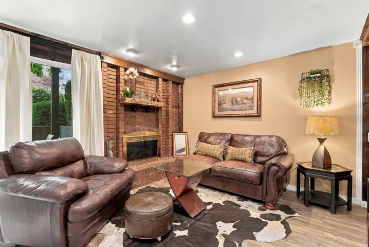 Brick fireplace with hearth, recessed lighting, wood-finish flooring, and large windows