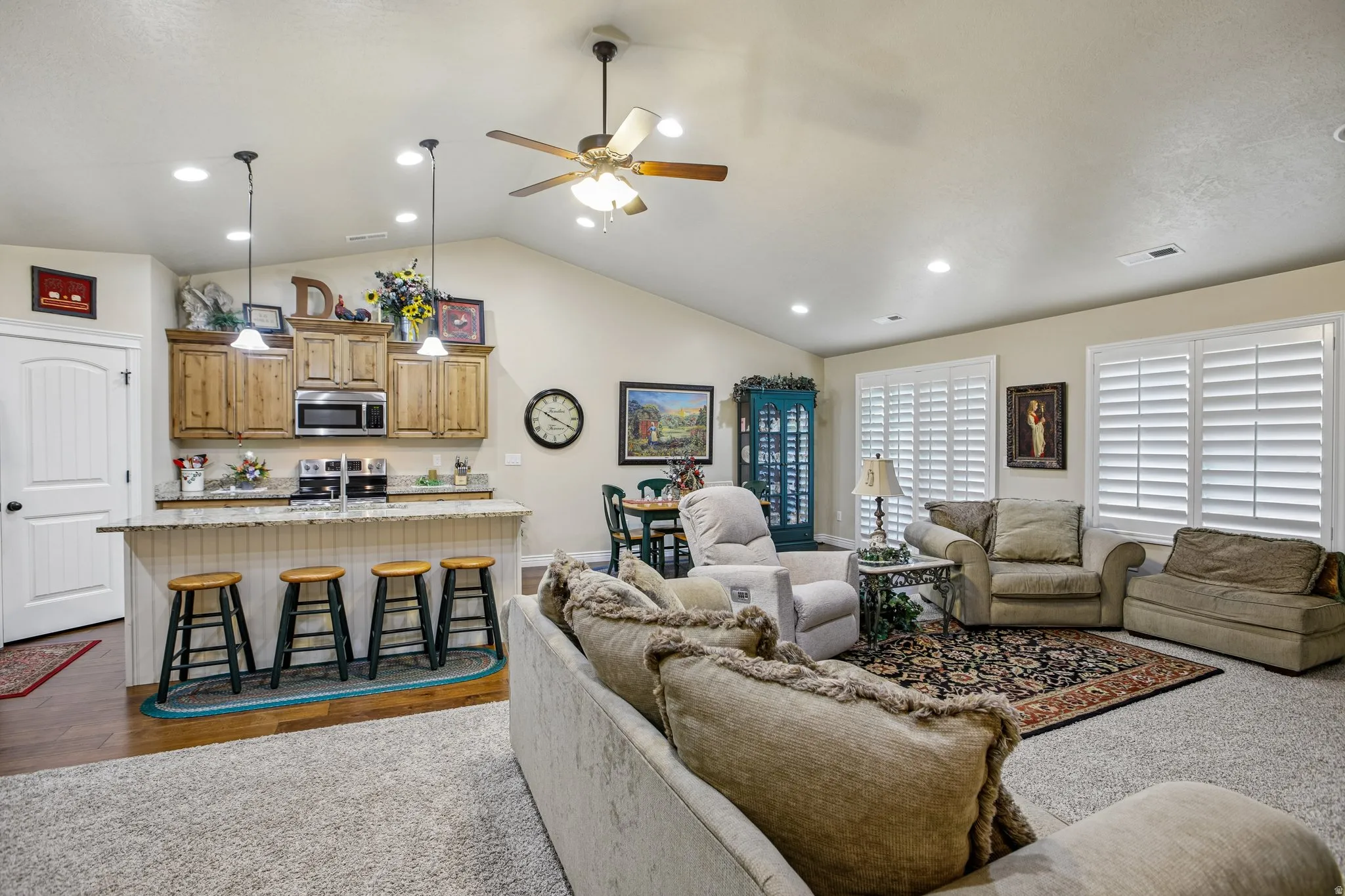 Vaulted ceilings with recessed lighting, wood-finish cabinetry, stainless steel kitchen appliances, a kitchen island with seating, and plantation shutters