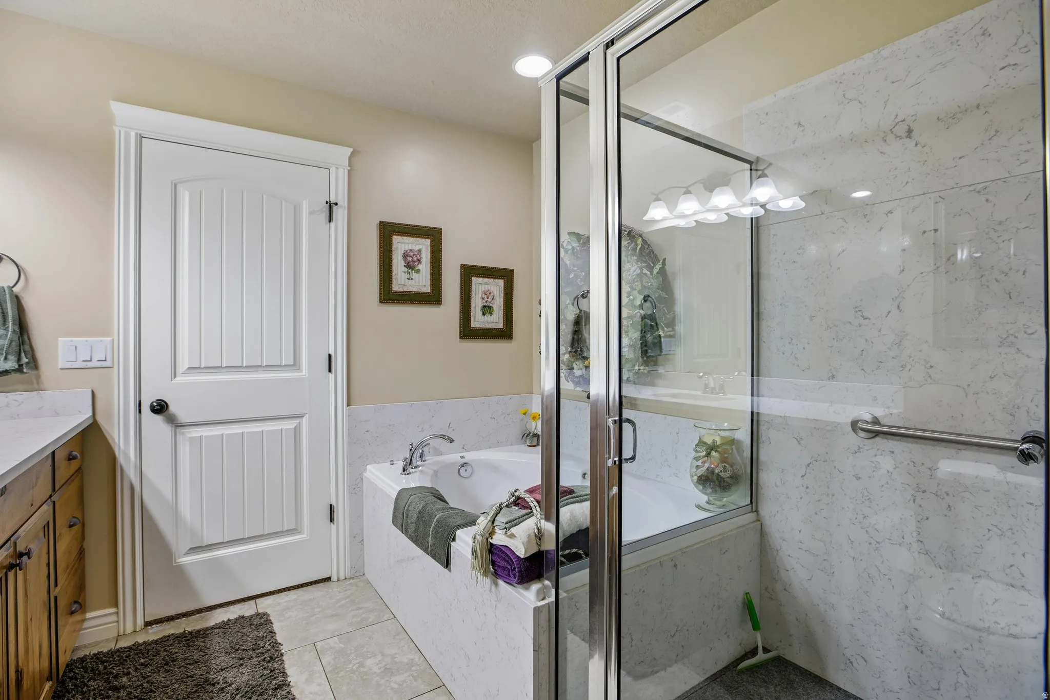 Built-in soaking tub, glass-enclosed shower, wood-finish vanity with countertop, and ceramic tile flooring