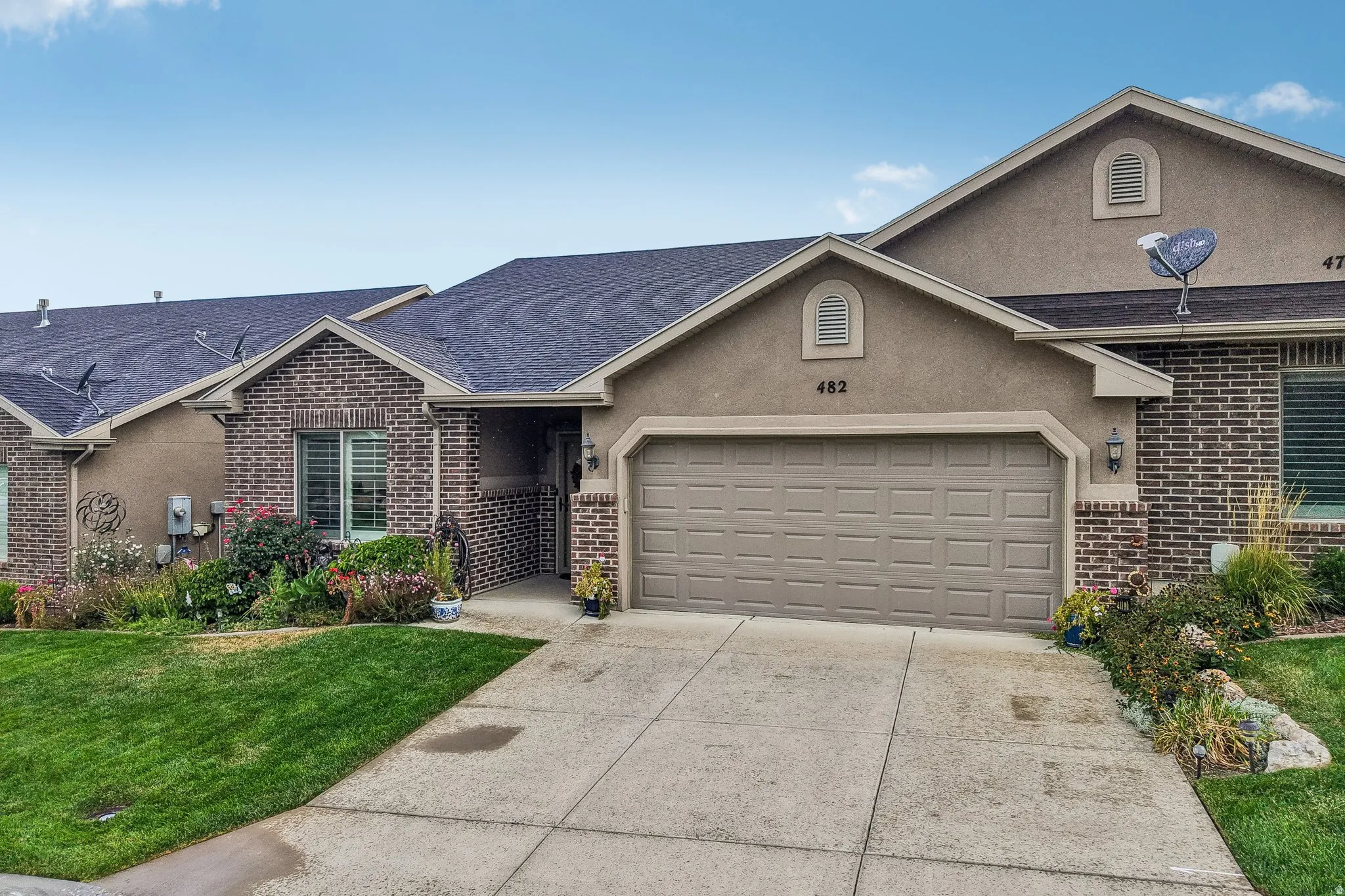 Brick and stucco exterior, dark asphalt shingle roof, attached garage with panel door, concrete driveway, and established landscaping