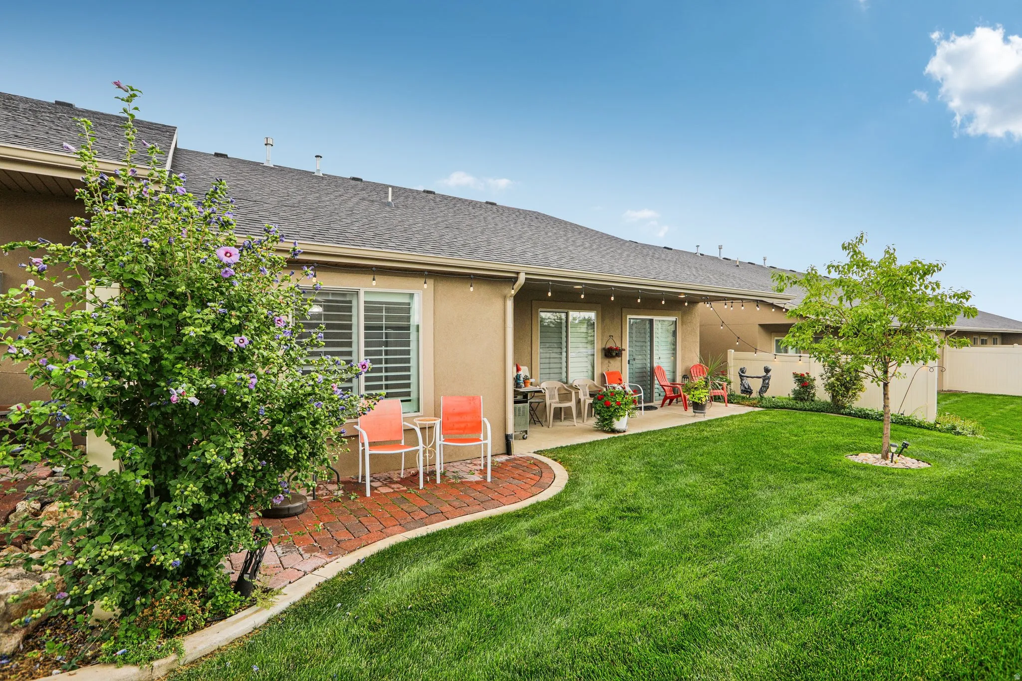 Expansive grassy yard with mature trees, a concrete patio, brick paver path, and sliding glass doors