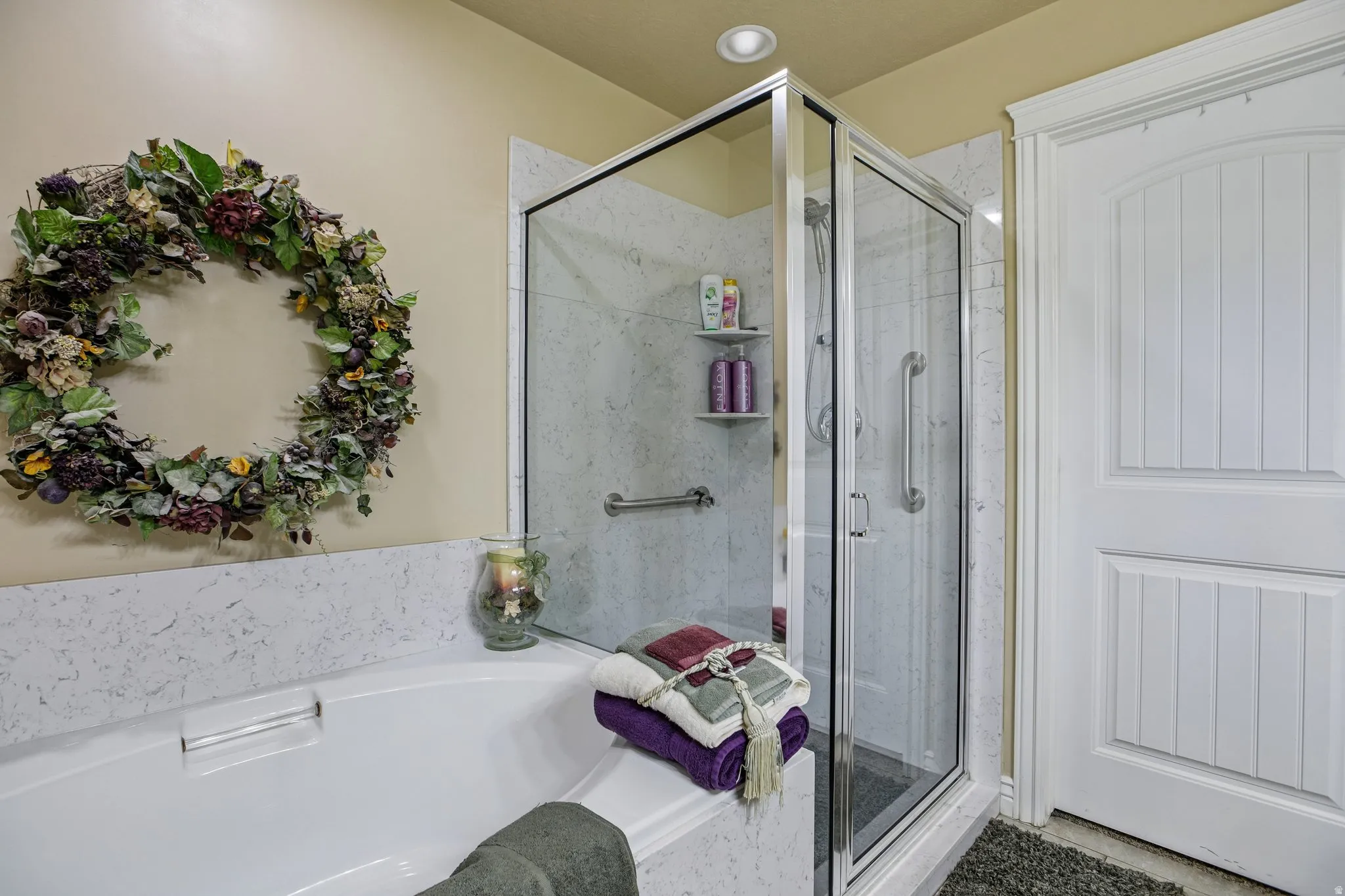 Walk-in shower with clear glass enclosure and grab bars, alongside a built-in bathtub with a composite surround