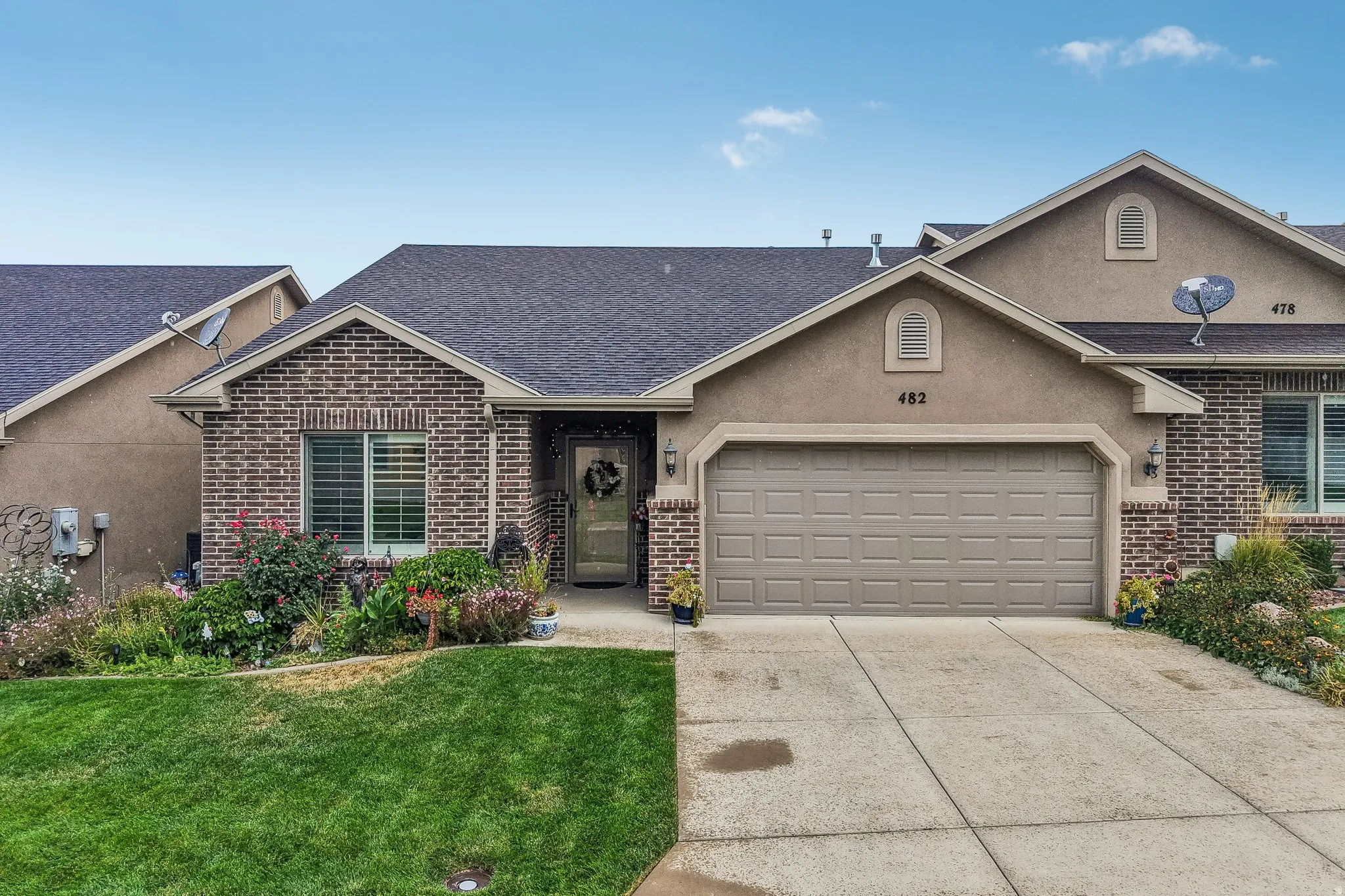 Brick and stucco exterior with an attached garage, paved driveway, and mature landscaping