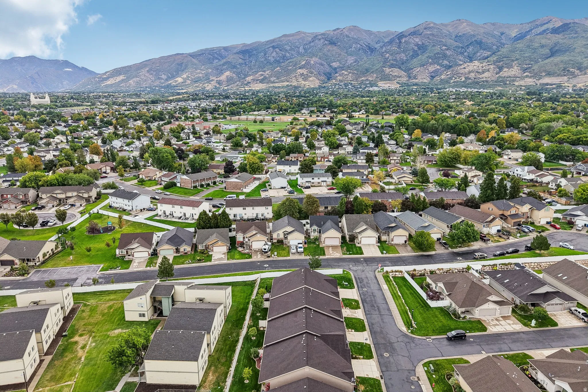Aerial perspective showcasing a residential community with abundant green spaces and mature trees, set against a mountainous backdrop