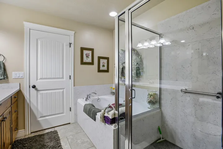 Built-in soaking tub, glass-enclosed shower, wood-finish vanity with countertop, and ceramic tile flooring