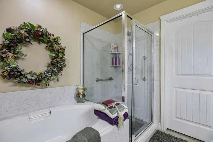 Walk-in shower with clear glass enclosure and grab bars, alongside a built-in bathtub with a composite surround