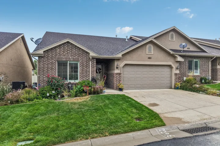 Exterior featuring a combination of brick and stucco finishes, an attached garage with a paved driveway, and a front yard with mature landscaping