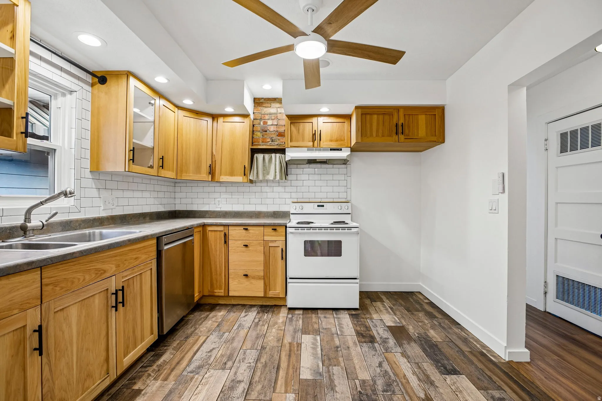 Kitchen with wood-finish flooring, wood cabinetry with black hardware, subway tile backsplash, and a ceiling fan with integrated lighting