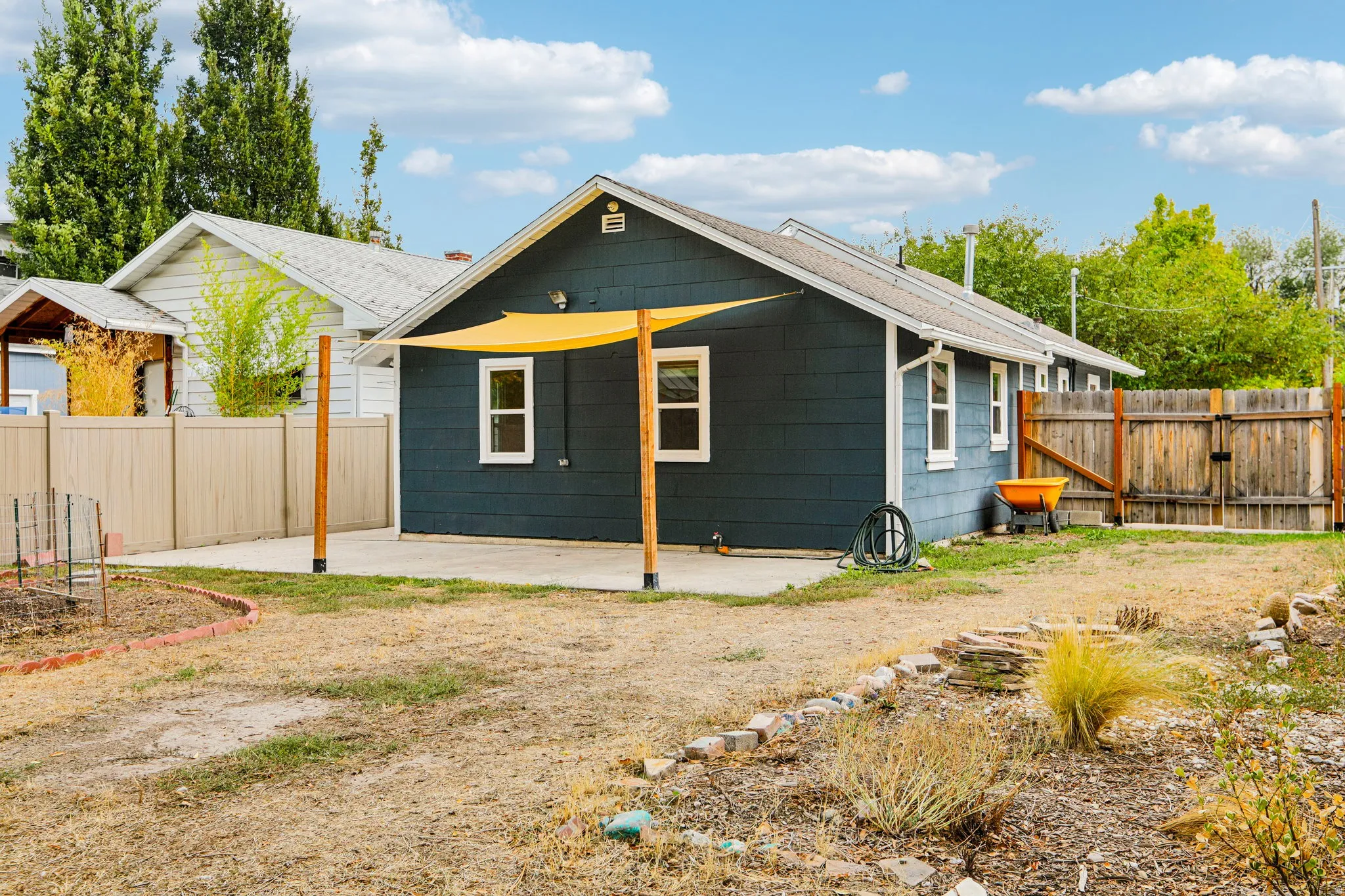 Rear exterior with blue siding, white trim windows, concrete patio, and a privacy fence