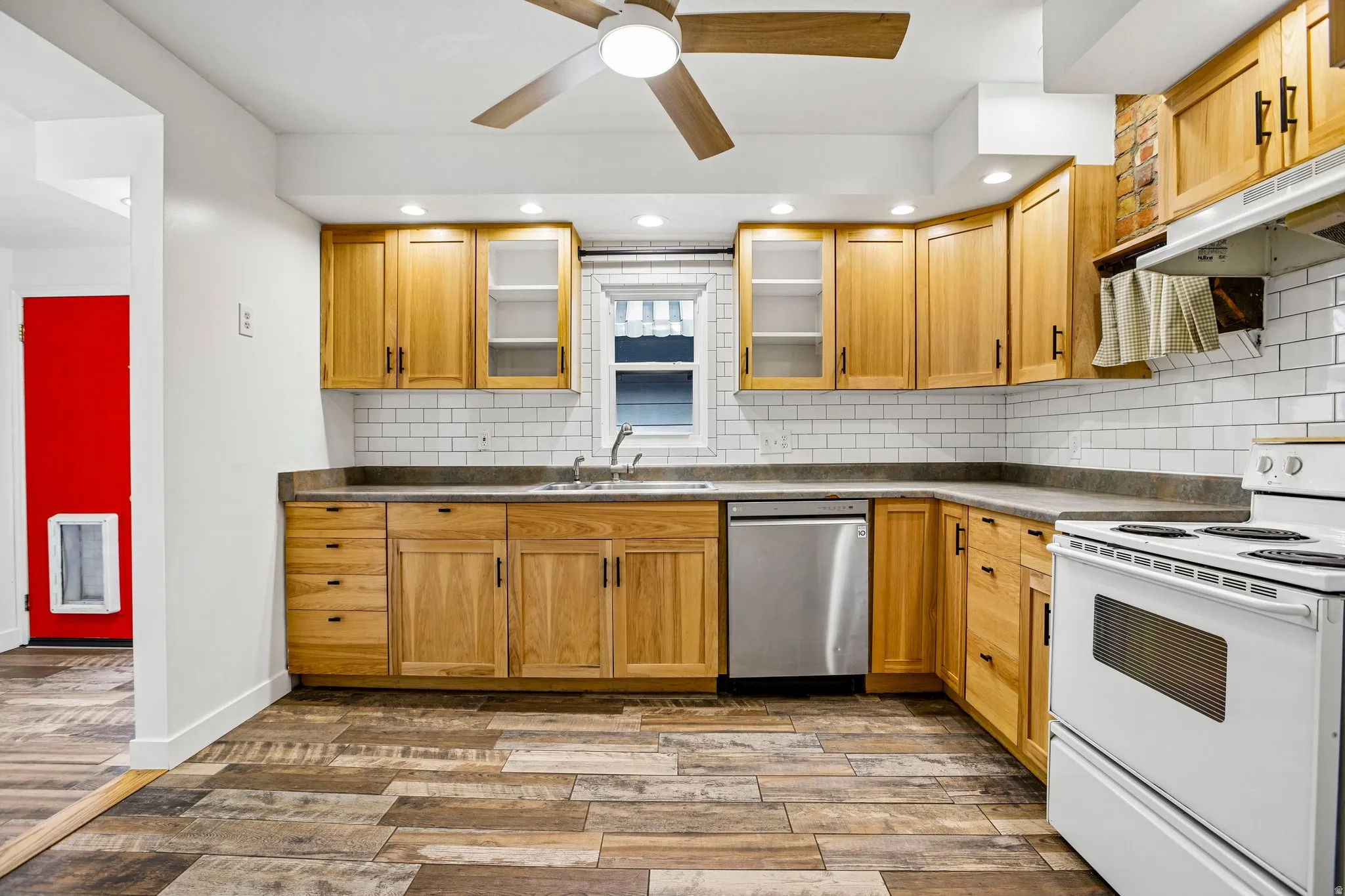 Kitchen featuring wood-finish flooring, wood cabinetry, subway tile backsplash, and a stainless steel dishwasher