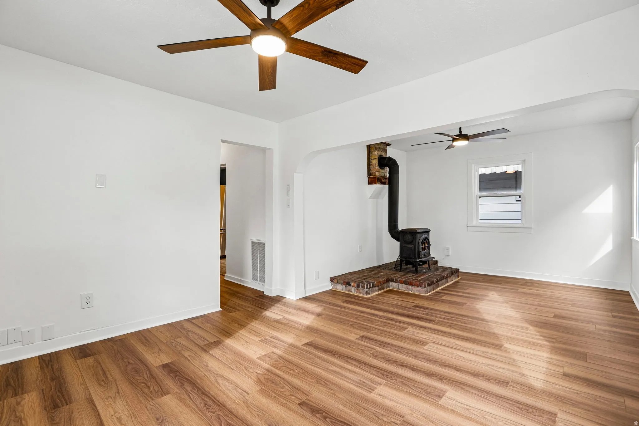 Wood-finish flooring throughout, bright white walls, and a wood-burning stove with a brick hearth