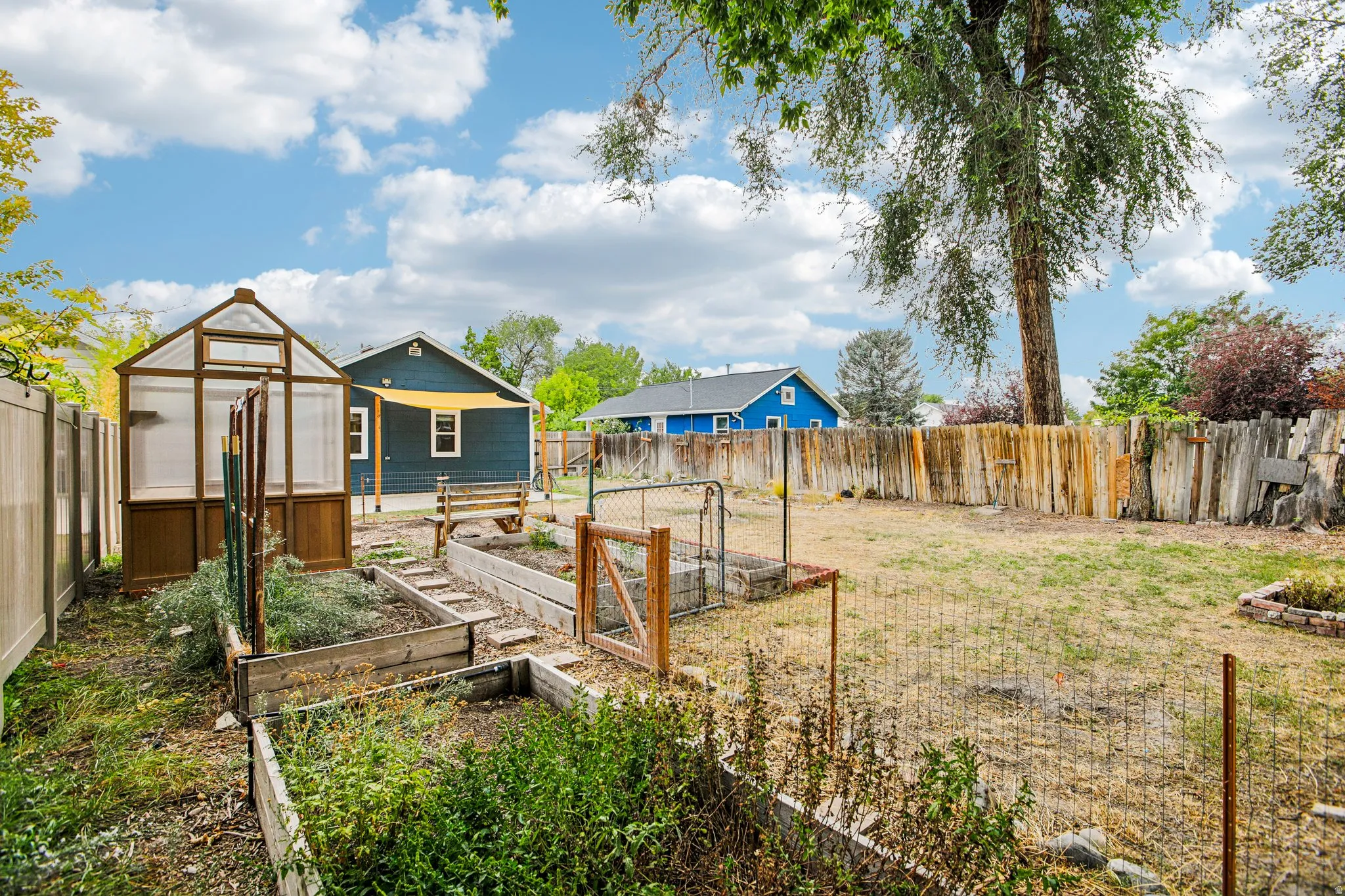 Expansive backyard featuring a greenhouse structure, raised garden beds, and a combination of wood and chain-link fencing